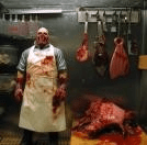 Haunted house butcher animatronic wearing bloody apron with hanging meat props
