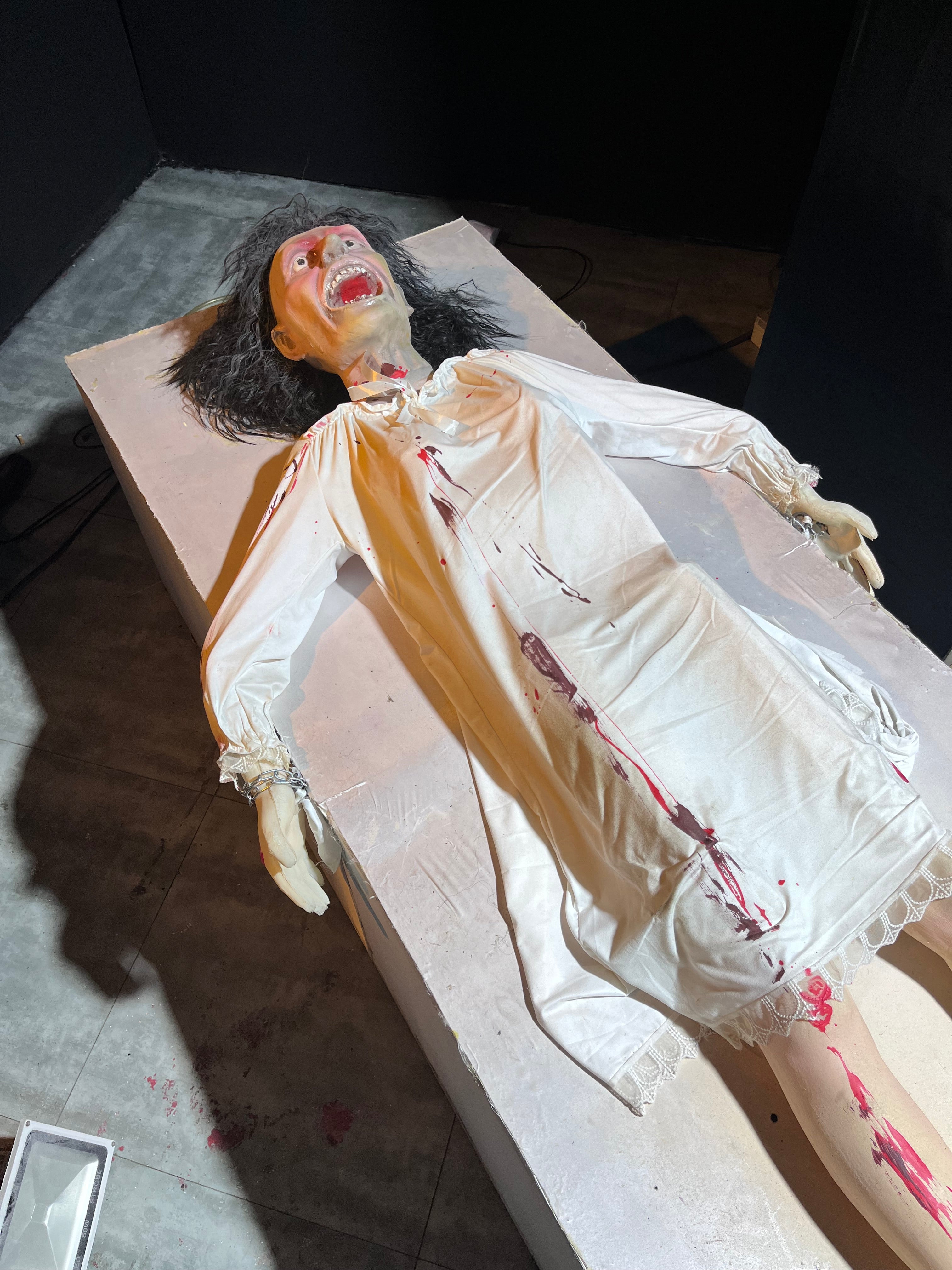 Animatronic psychiatric patient in yellow gown twisting on hospital bed for haunted attraction