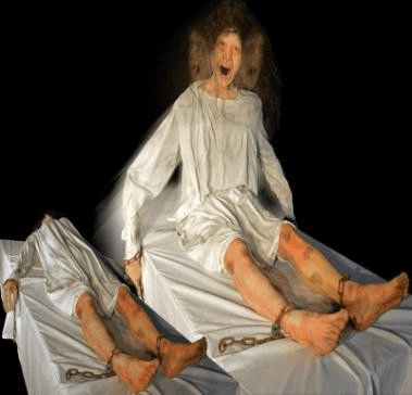 Animatronic psychiatric patient in yellow gown twisting on hospital bed for haunted attraction